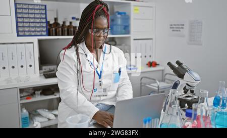 Scienziata afroamericana concentrata impegnata in una seria ricerca medica sul suo portatile in laboratorio, ritratto di un bellissimo adulto con trecce consegnare Foto Stock