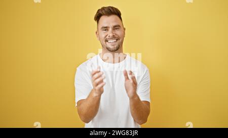 Un giovane sorridente barbuto che batte le mani su un vibrante sfondo giallo. Foto Stock