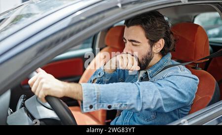 Giovane uomo ispanico stanco di guidare l'auto sbadigliando in strada Foto Stock