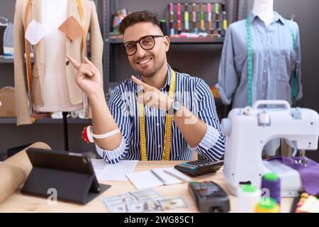 Uomo ispanico con barba disegnatore di sarte che lavora presso l'atelier sorridente e guarda la fotocamera che punta con due mani e dita di lato. Foto Stock