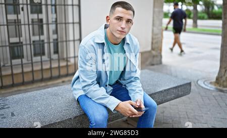 Uomo ispanico seduto sulla panchina che usa lo smartphone in un ambiente urbano Foto Stock
