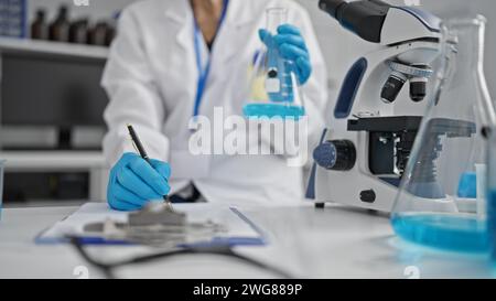 Sguardo intrigante alle mani esperte di una scienziata anziana che prende appunti meticolosamente in laboratorio, immersa nel suo straordinario esperto di provette Foto Stock