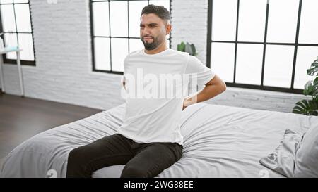 Un uomo doloroso che si aggrappa e si tiene le spalle in una camera da letto moderna Foto Stock