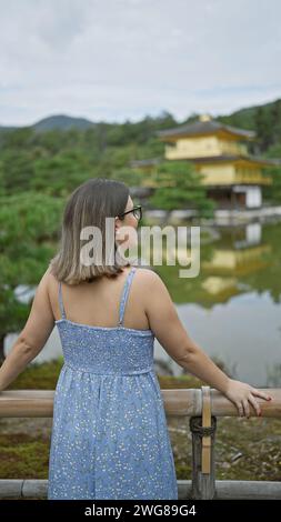 Gioiosa donna ispanica con occhiali che ammirano il padiglione dorato di kinkaku-ji, il suo bel sorriso radioso mentre gode della vista mozzafiato di kyoto, giappone. Foto Stock