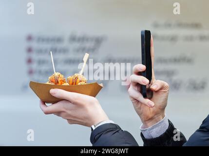 Le mani delle donne tengono il dessert e il telefono cellulare, la parte centrale del corpo delle donne si fanno un selfie del dessert con uno spazio per le copie, il mercato del cibo di strada degli agricoltori a Pragu Foto Stock