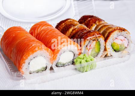 Una varietà di sushi roll, tra cui salmone e anguilla, serviti in un contenitore di plastica con wasabi, pronti per il prelievo o la consegna. Foto Stock