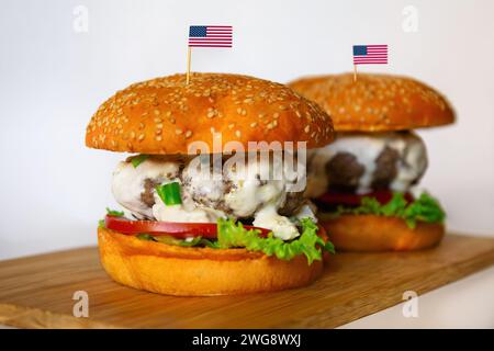 Due cheeseburger con panini di sesamo, adornati con bandiere americane, su una tavola di legno Foto Stock