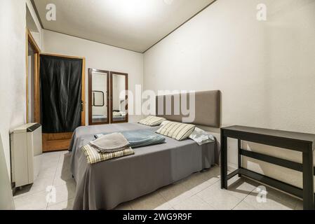 Camera da letto di una casa con due letti di diverse altezze, testiera rivestita in tessuto, alcuni specchi sulle pareti e porta in legno che conduce ad una Foto Stock