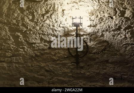 Torcia del castello medievale illuminata appesa a un muro di pietra, oggetti d'epoca e sfondo Foto Stock