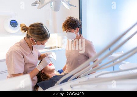 Dentista e assistente che esegue un controllo della bocca e dei denti su un cliente nella moderna clinica dentale Foto Stock