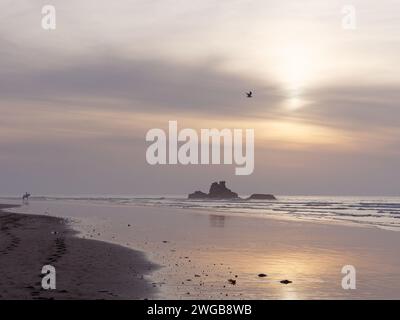 Tramonto su un affioramento roccioso su una spiaggia di Essaouira con un solitario cavaliere e impronte sulla spiaggia di sabbia, Marocco, 3 febbraio 2024 Foto Stock