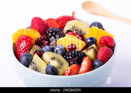 Macedonia di frutta fresca mista in un recipiente con un cucchiaio di legno in primo piano. Sfondo bianco Foto Stock