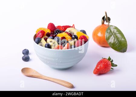 Macedonia di frutta fresca mista in un recipiente con un cucchiaio di legno in primo piano. Sfondo bianco Foto Stock