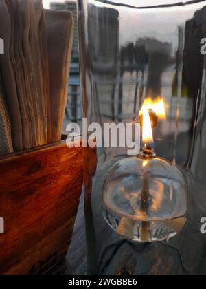 Lampada da tavolo a lanterna ad olio, vetro trasparente, luce romantica sul tavolo in legno, ristorante dall'atmosfera calda, primo piano, tavolo da pranzo con carta velina Foto Stock