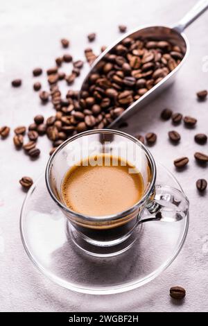 In primo piano una tazza di vetro trasparente con caffè espresso italiano, sullo sfondo chicchi di caffè tostati Foto Stock