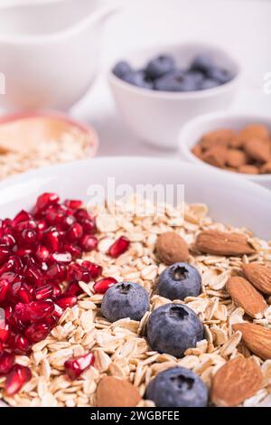 ciotola con avena arrotolata, mirtilli, semi di melograno e mandorle in primo piano con una concentrazione selettiva Foto Stock