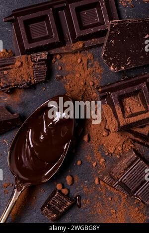 in primo piano, in un ambiente buio, cacao in polvere, pezzi di cioccolato fondente e cioccolato fuso Foto Stock