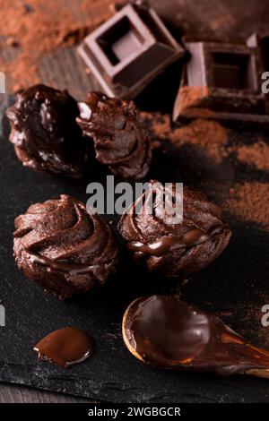 in primo piano, in un ambiente buio, alcuni baci al cioccolato, polvere di cacao e pezzi di cioccolato fondente. Foto Stock