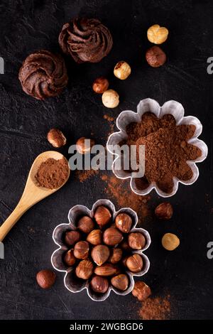 vista dall'alto. Stampi in alluminio per torte con nocciole e cacao in polvere e alcuni baci al cioccolato su sfondo scuro e testurizzato. Foto Stock