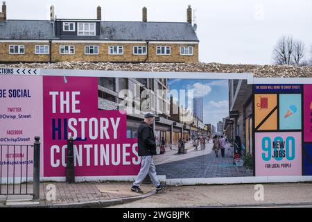 L'uomo locale cammina accanto al cartellone per la rigenerazione delle abitazioni e al mucchio di macerie al Chrisp Street Market di Poplar, Tower Hamlets, East London. Foto Stock