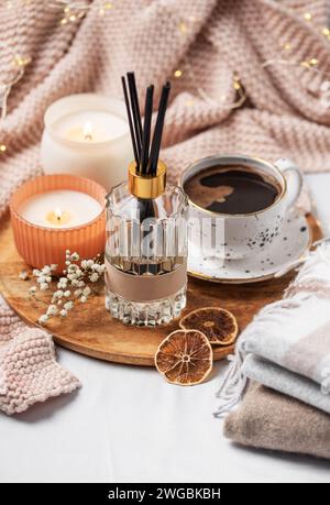 Bastoncini di bambù in bottiglia con candele profumate e una tazza di caffè sul letto. Atmosfera accogliente. Foto Stock