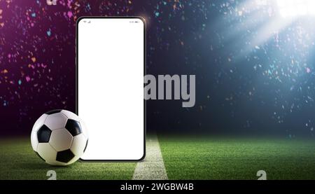 Smartphone vuoto e pallina da calcio sul campo dello stadio: App per le scommesse sportive e per i campionati di calcio Foto Stock