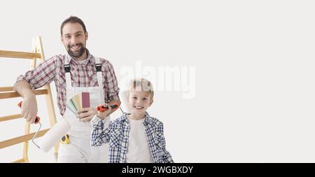 Padre e figlio che dipingono insieme la loro nuova casa, tengono i rulli di vernice e sorridono alla macchina fotografica Foto Stock