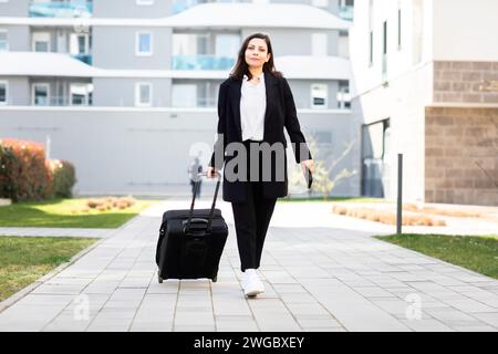 Donna che passa davanti a un condominio che tira bagagli su ruote, in Germania Foto Stock