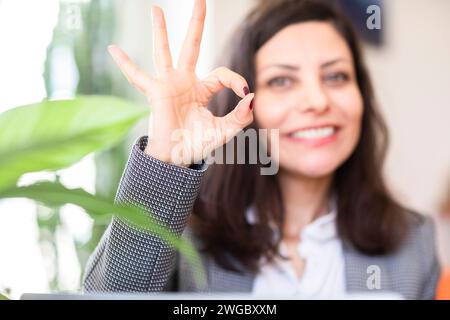 Donna d'affari sorridente seduta in un ufficio che fa un buon segno Foto Stock