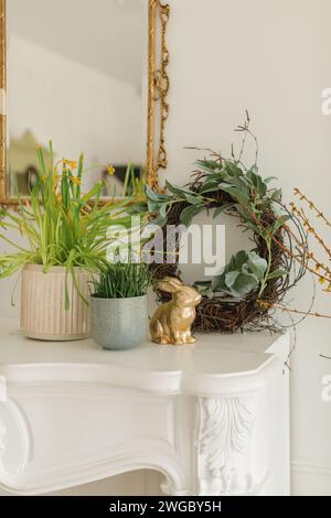 Festiva coniglietto di Pasqua dorato, corona e piante d'uva primaverile su un manipolo sotto uno specchio Foto Stock