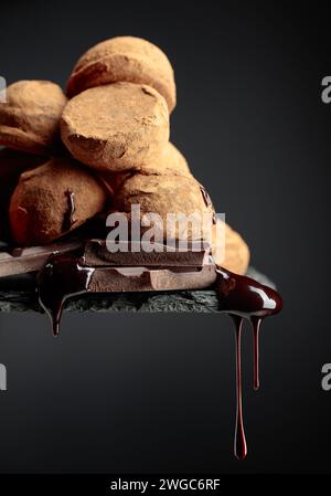 Deliziosi tartufi di cioccolato e gocce di salsa di cioccolato su sfondo nero. Foto Stock