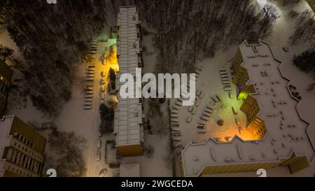 Fotografia con drone di parcheggio vicino a un edificio e auto coperte di neve durante la mattina nuvolosa d'inverno Foto Stock