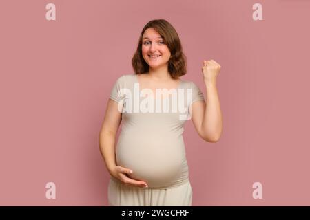 Una donna incinta di successo su uno sfondo rosa studio. Gravidanza in una donna contenta con la pancia Foto Stock