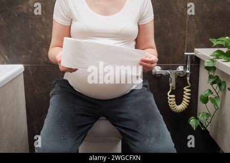 Una donna incinta è seduta sul gabinetto con la carta igienica in mano Foto Stock