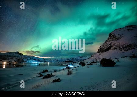 Pittoresco scenario dell'aurora boreale o dell'aurora boreale che si illumina sulle montagne innevate sulla costa in inverno alle isole Lofoten, Norvegia Foto Stock