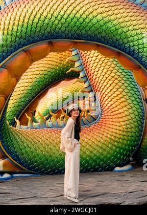 Giovane turista asiatica in piedi e in posa per una foto con il corpo di colorata scultura serpente nel tempio buddhista in Thailandia Foto Stock