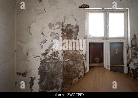 Una camera caratterizzata da pavimento in legno e pareti sbucciate in una vecchia citta' deserta Foto Stock