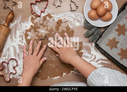 Vista dall'alto della donna che taglia l'impasto con le frese per biscotti natalizi sul tavolo e le prepara su un vassoio da forno Foto Stock