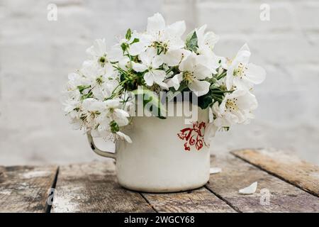 Natura morta con tazza e bouquet di rami con fiori di mele. Petali bianchi di alberi in fiore caduti su cemento. Foto Stock