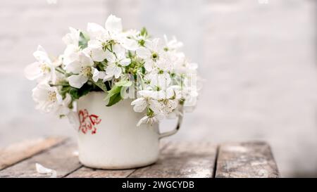 Natura morta con tazza e bouquet di rami con fiori di mele. Petali bianchi di alberi in fiore caduti su cemento. Foto Stock