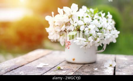 Natura morta con tazza e bouquet di rami con fiori di mele. Petali bianchi di alberi in fiore caduti su cemento. Foto Stock
