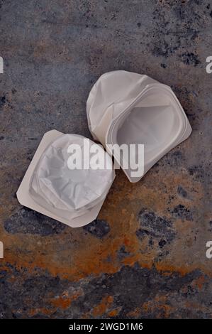 Due vasi vuoti di yogurt di plastica bianca spalmati appoggiati su metallo arrugginito Foto Stock