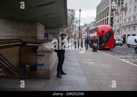 Uomo che legge un libro mentre aspetta fuori dalla stazione della metropolitana di Green Park, a Piccadilly, Londra, Inghilterra, Regno Unito Foto Stock