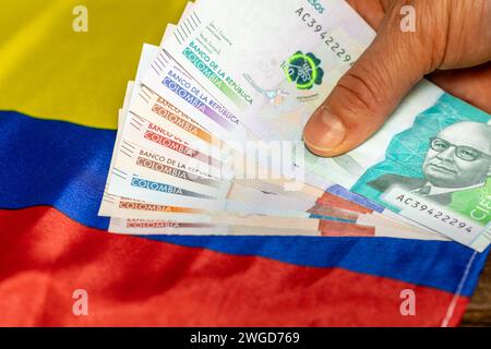 Un mucchio di pesos colombiani tenuti in mano sullo sfondo della bandiera della Colombia, Business Concept, analisi economica, potere d'acquisto del denaro Foto Stock