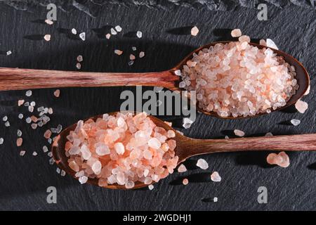 Due cucchiai di legno adagiati su un'ardesia sono riempiti di sale rosa Foto Stock