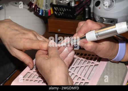 Il manicurista tiene le dita del cliente in mano e affila le unghie con una fresa. Foto Stock