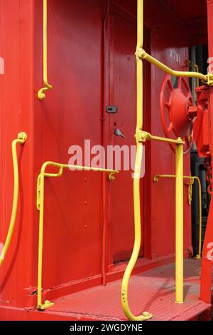 Una fotografia sorprendente cattura il contrasto tra il corpo rosso e il corrimano giallo di una carrozza ferroviaria, sottolineandone i colori audaci Foto Stock
