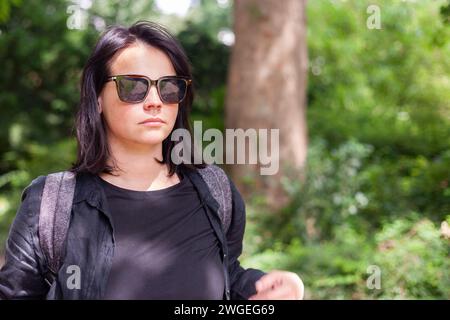 Ritratto di una bella giovane donna che indossa gli occhiali da sole e cammina nel parco Foto Stock