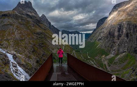 Un turista si trova sulla piattaforma panoramica di Trollstigen in Norvegia, affascinato dalle ampie vedute delle strade serpentine che tagliano la gola Foto Stock