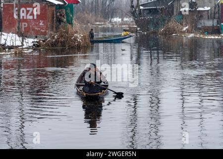 Srinagar, India. 4 febbraio 2024. Un uomo fila la sua barca sul lago dal durante le nevicate. Le pianure del Kashmir stanno assistendo a una moderata nevicata, mentre nei tratti più alti della valle sono state segnalate forti nevicate. La valle del Kashmir ha subito una nevicata fresca che ha sconvolto la normale vita delle persone. Le operazioni di volo, il trasporto di superficie e le attività di routine della vita si arrestarono. (Immagine di credito: © Idrees Abbas/SOPA Images via ZUMA Press Wire) SOLO USO EDITORIALE! Non per USO commerciale! Foto Stock